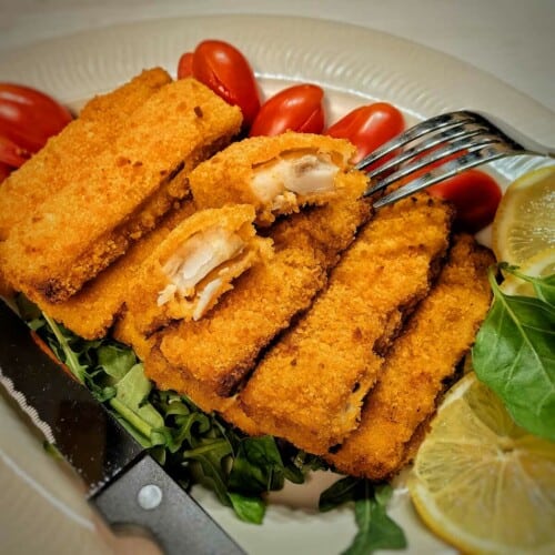 air fryer frozen fish sticks on a bed of greens with tomatoes, lemon slice and utensils