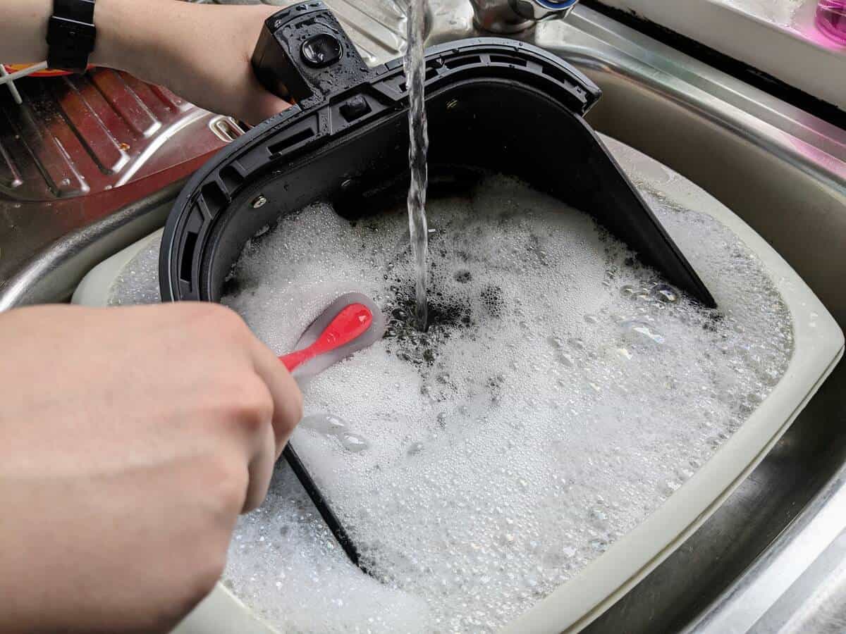 washing air fryer basket in the sink with soapy water