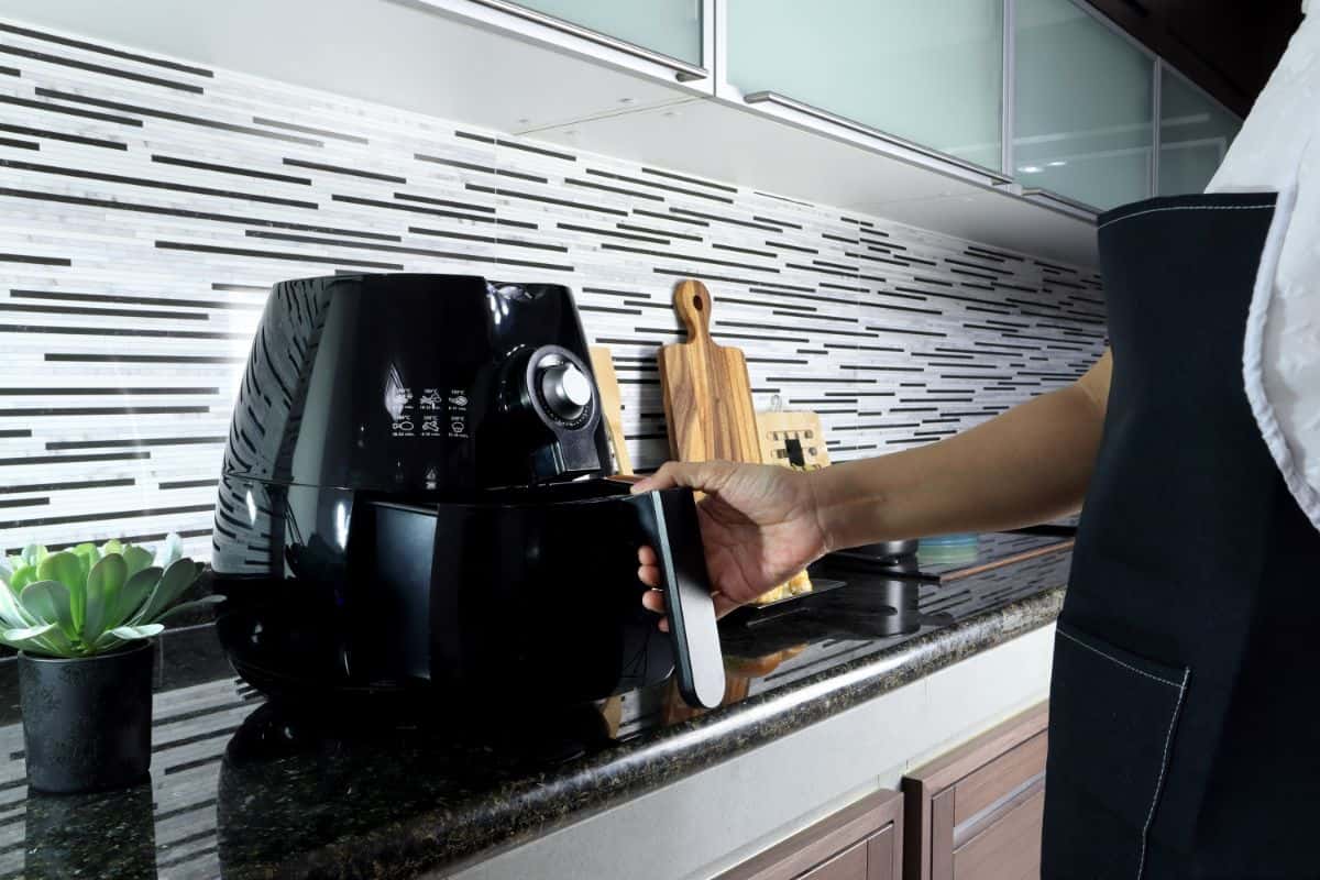 man with apron using air fryer on the countertop