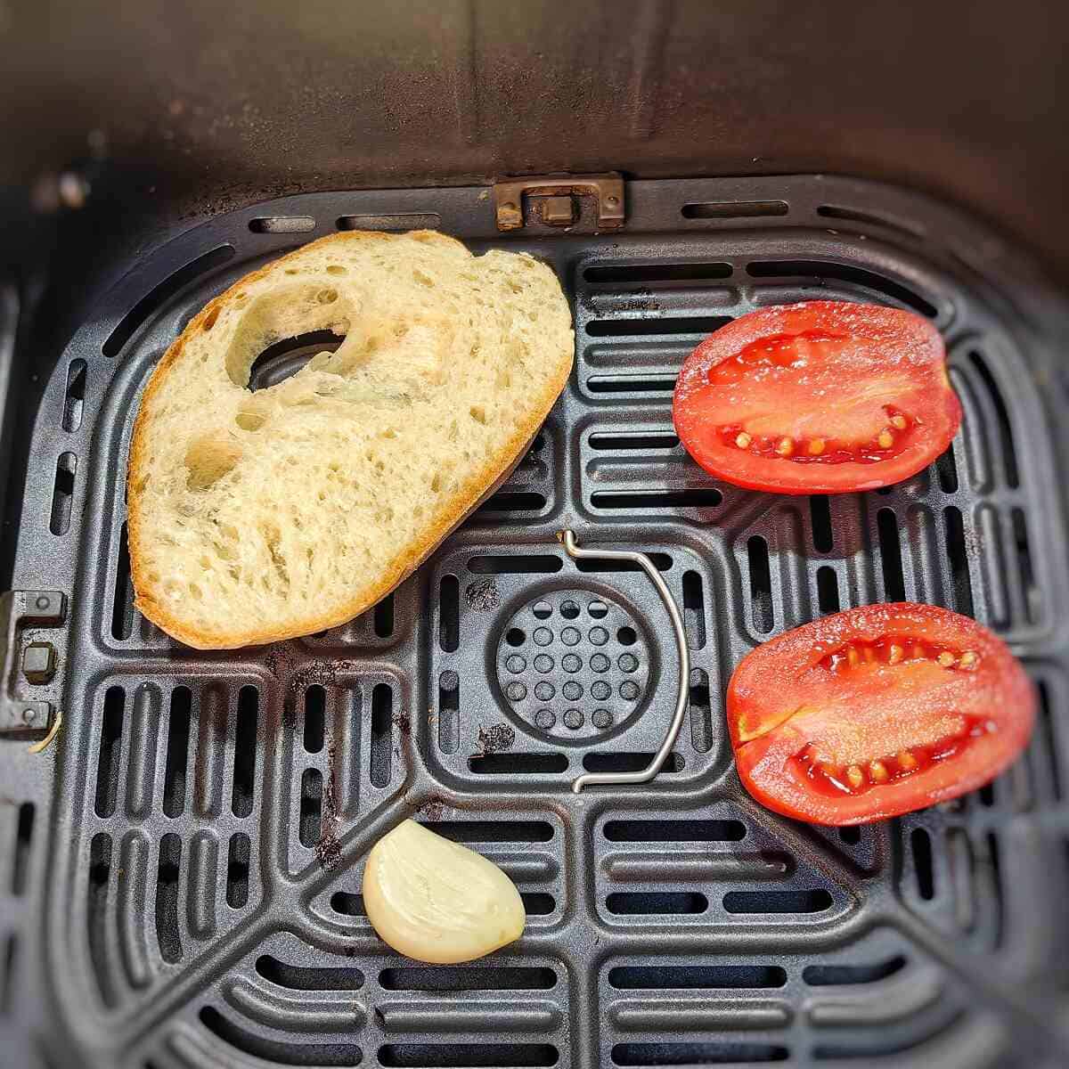 tomato halves, garlic clove and bread inside air fryer basket