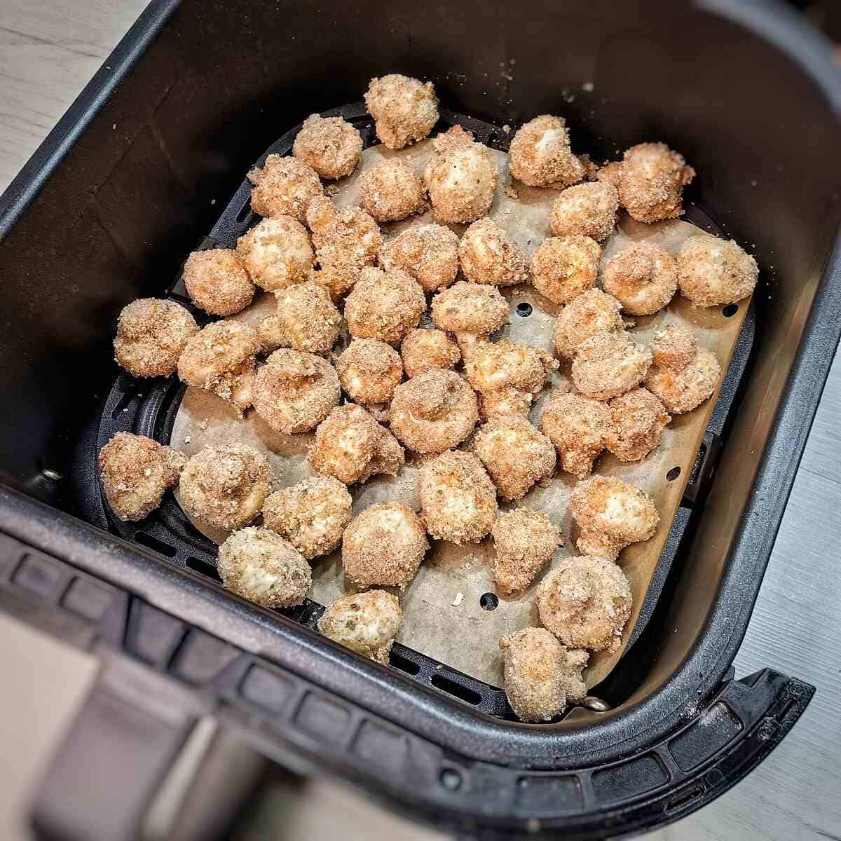 breaded mushrooms inside parchment-lined air fryer basket