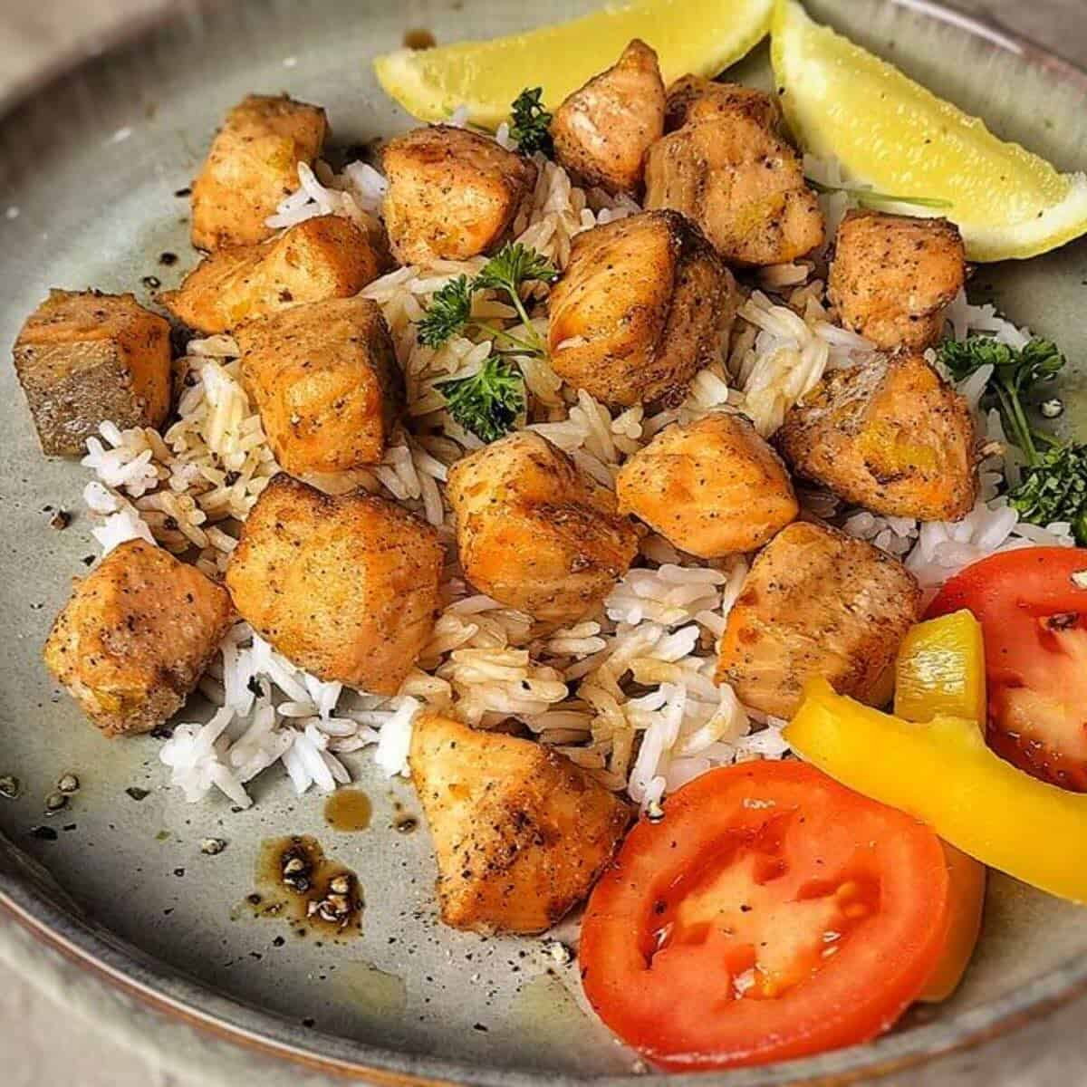 salmon bites on a bed of rice with lemon wedges and sliced tomatoes