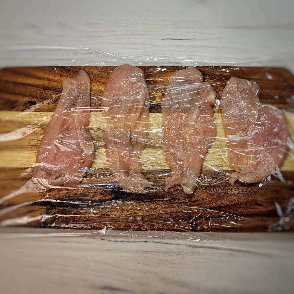 sliced chicken breasts with saran wrap on top