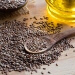 flaxseed on a wooden spoon, with flaxseed oil in the background