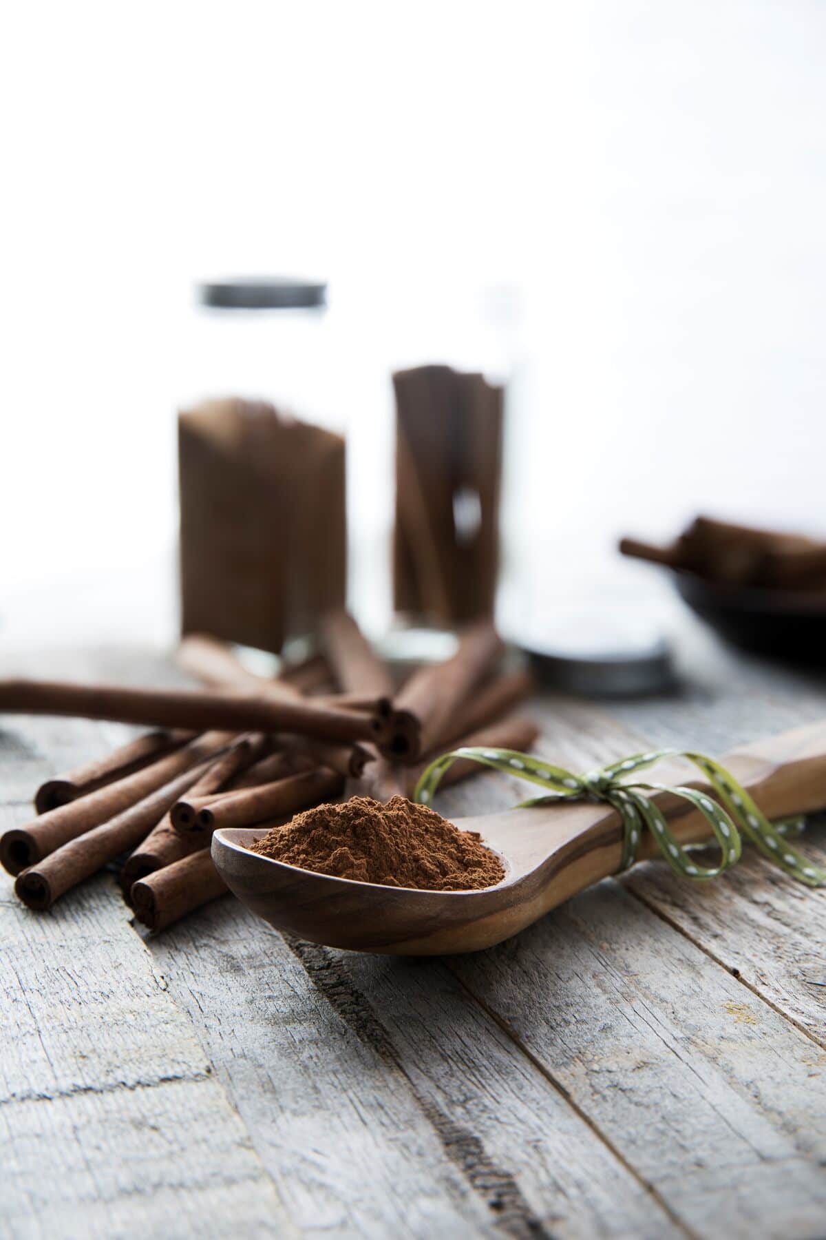 wooden spoon filled with ground cinnamon in front of cinnamon sticks.