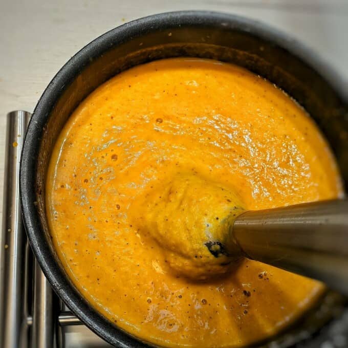 creamy pumpkin soup in a pot with immersion blender