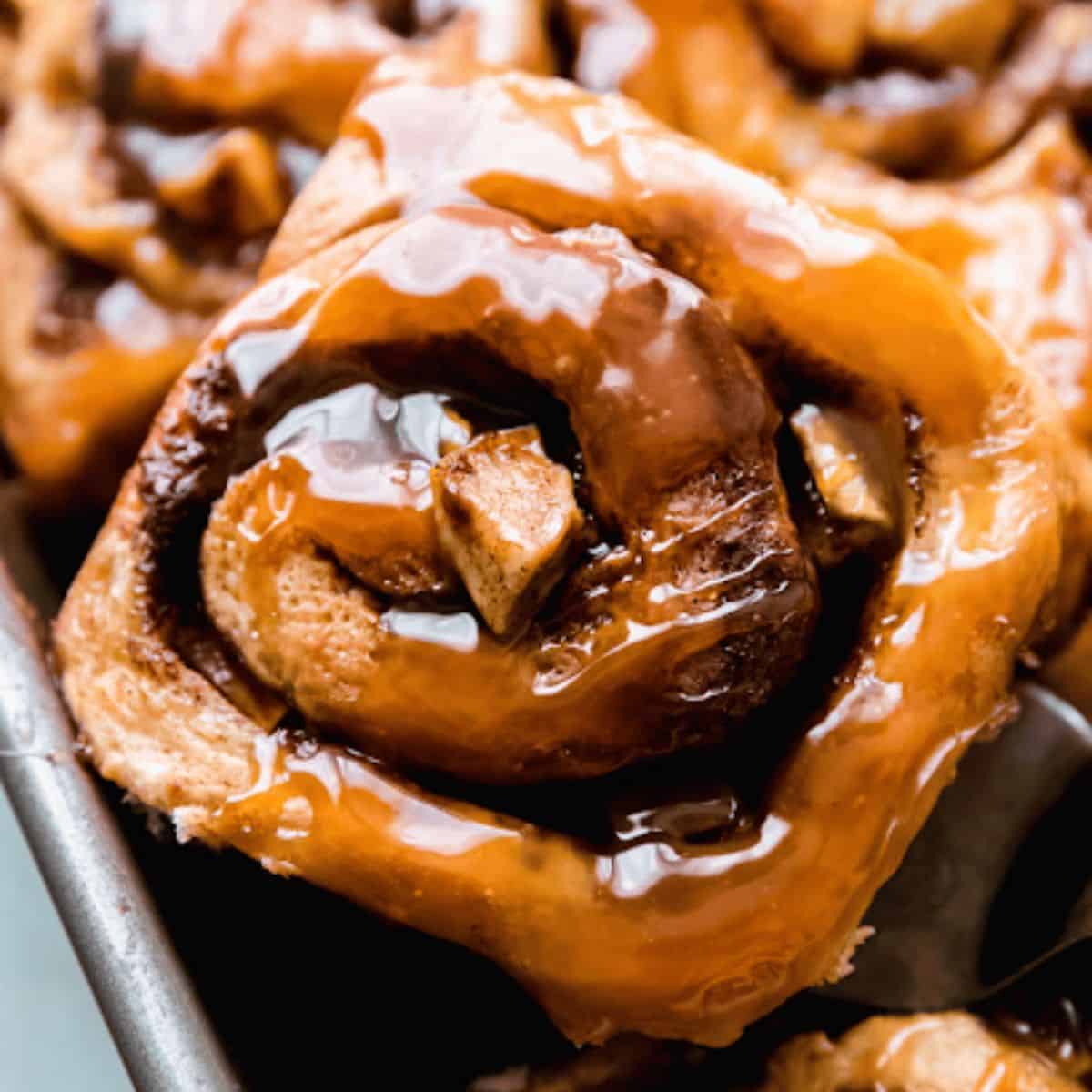 A tray of warm caramel apple cinnamon rolls, drizzled with gooey caramel sauce.