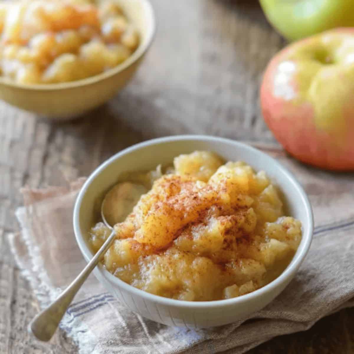 Chunky homemade apple sauce, filled with soft apple pieces and a hint of cinnamon, surrounded by fresh apples and a spoon, showcasing a delicious fall treat.