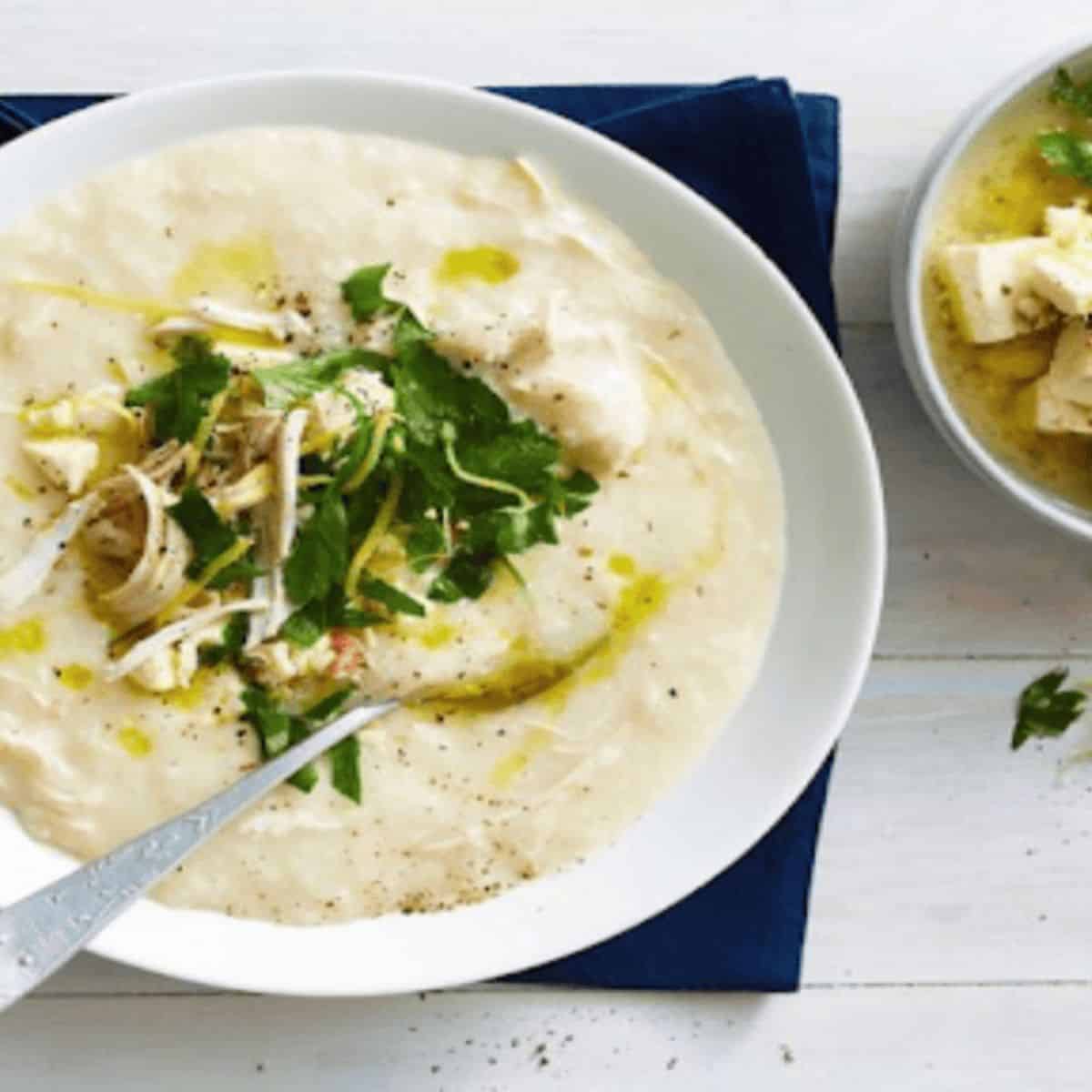 Delicious creamy Greek lemon soup set in a white bowl with a spoon and a salad on the side