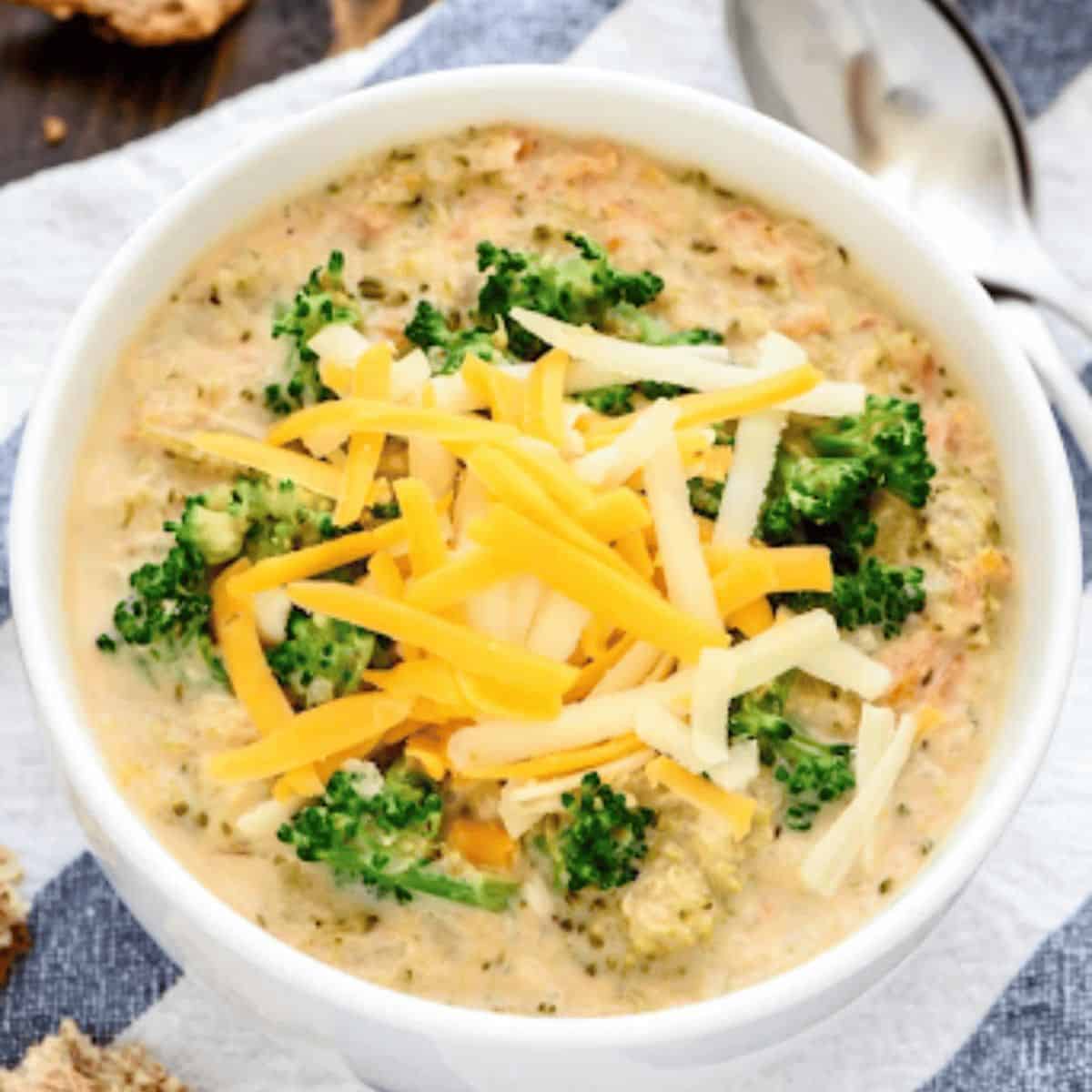 Delicious broccoli soup with 3 different types of cheese on top placed on a blue and white striped cloth
