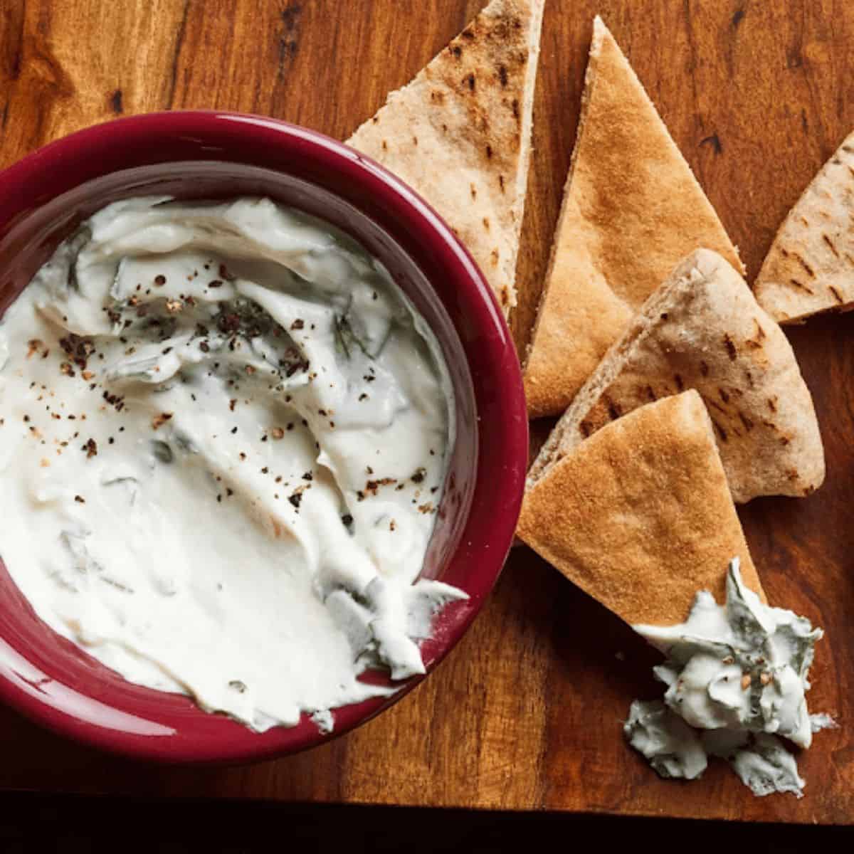 A creamy tahini yogurt dip served in a small bowl, garnished with a sprinkle of sesame seeds, surrounded by fresh tacos for dipping.