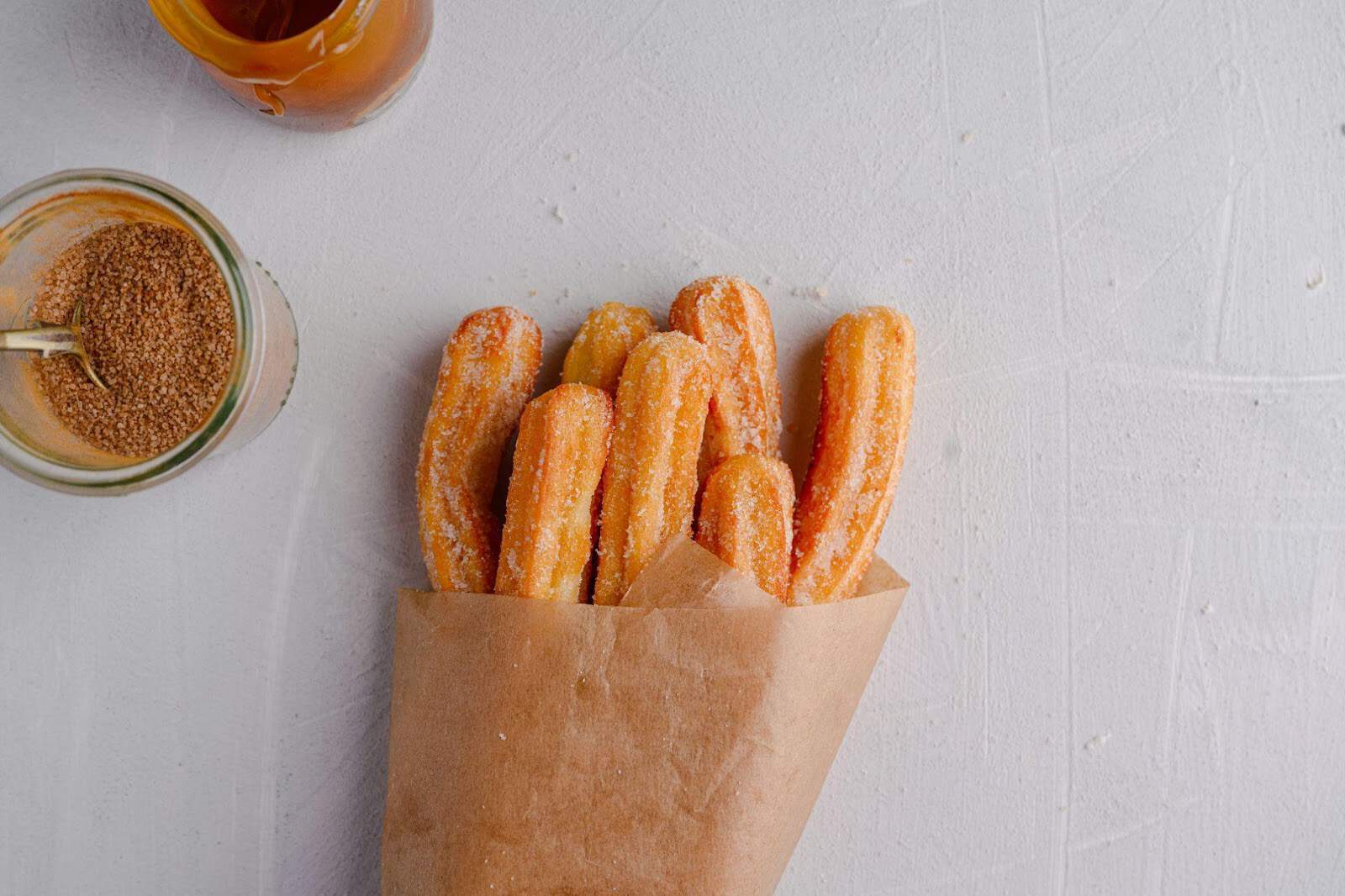 air fryer churros wrapped in a parchment paper with cinnamon and sugar in a glass container.