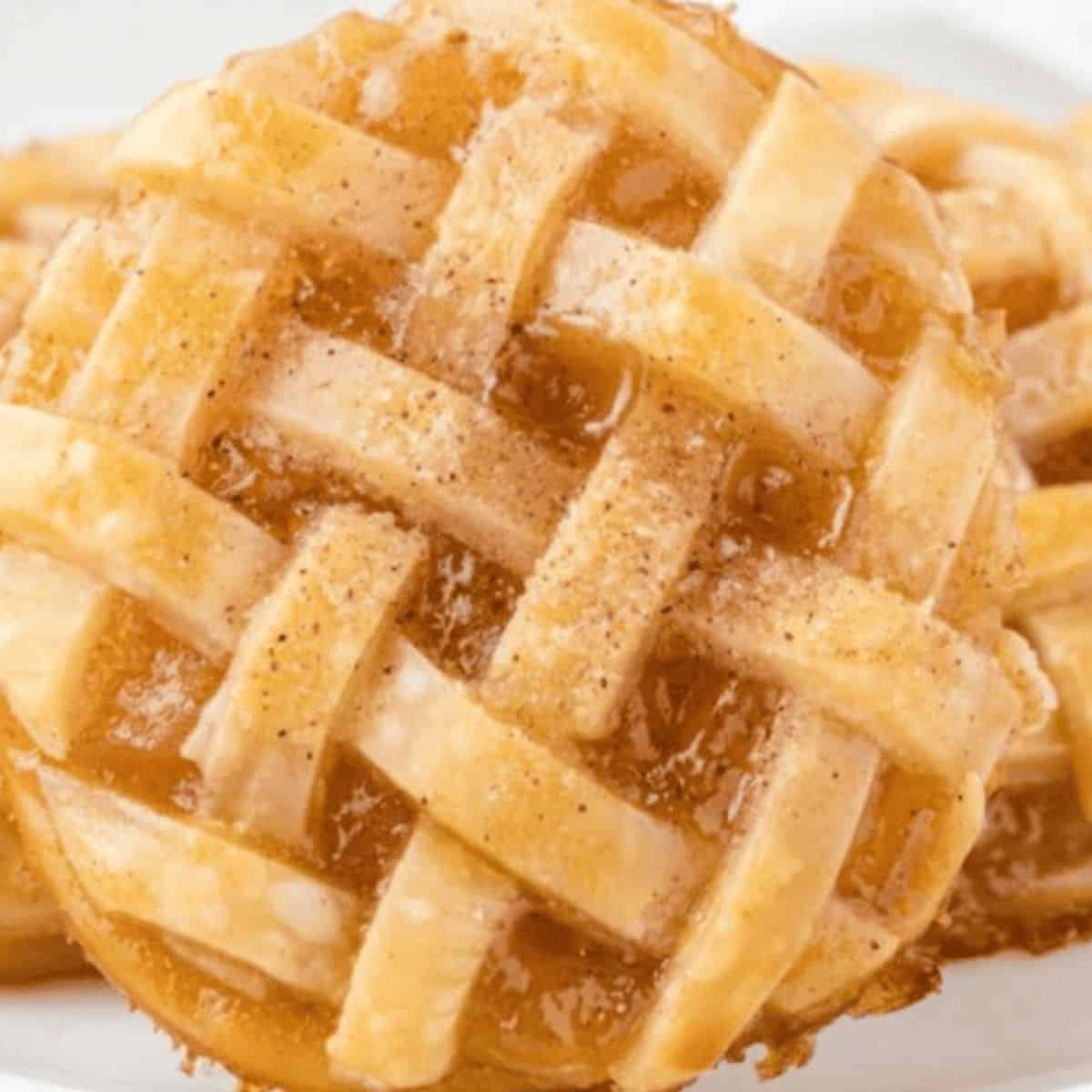 A plate of caramel apple pie cookies, featuring flaky crusts, warm apple filling, and a lattice top, dusted with sparkling sugar.
