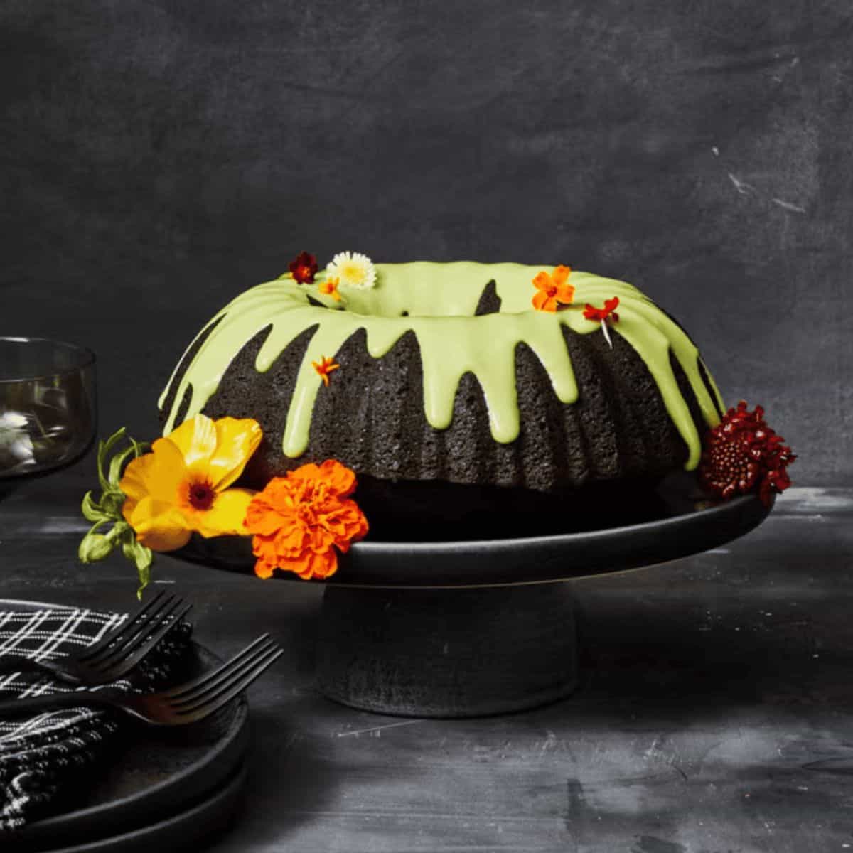A black cake on a cake tray decorated with a layer of icing and flowers making it look like a haunted cake.