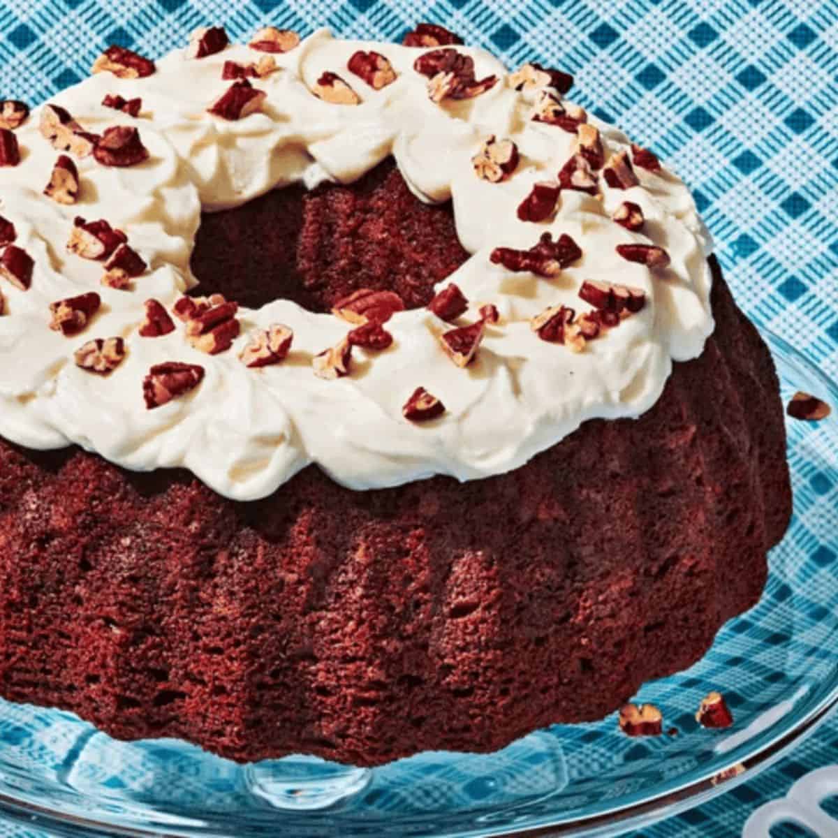 Moist butternut squash cake, topped with creamy frosting and garnished with a sprinkle pecan nuts, served on a decorative plate.
