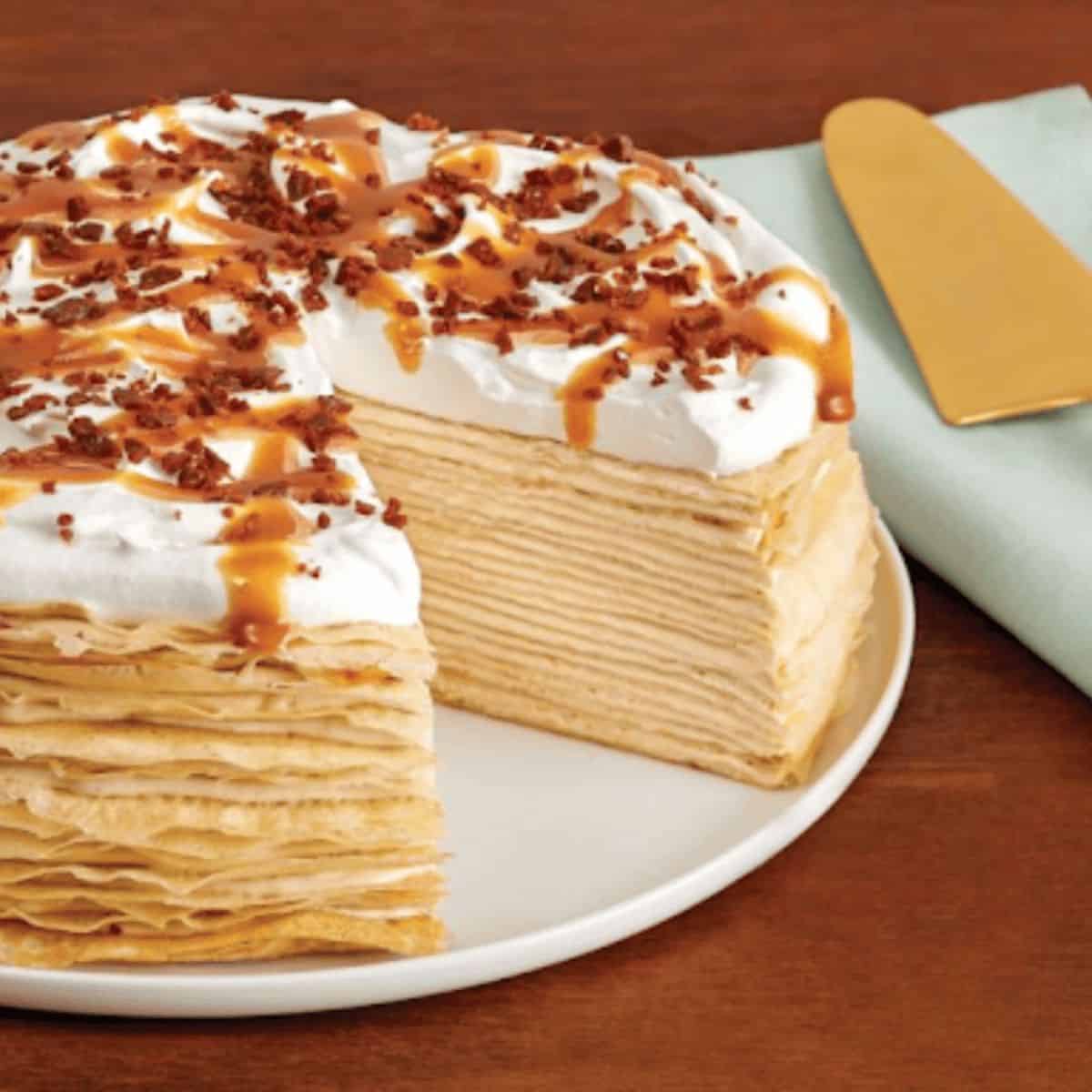 A stunning caramel-cinnamon crepe cake, featuring delicate layers of thin crepes filled with creamy caramel and cinnamon frosting, elegantly drizzled with caramel sauce on top and garnished with a sprinkle of cinnamon.