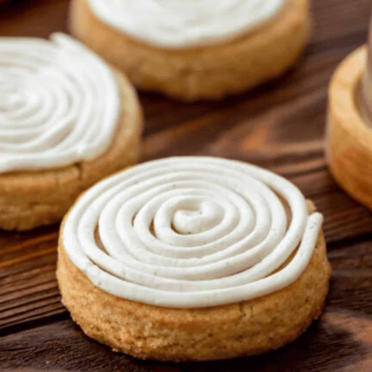 Soft Cinnamon Roll Sugar Cookies topped with creamy cream cheese frosting on a wooden table.