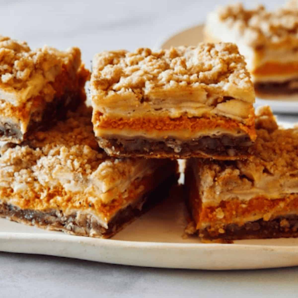 A plate of Every Flavor Thanksgiving Pie Bars, featuring layers of different pie fillings like pumpkin, pecan, and apple, all topped with a crumbly crust.