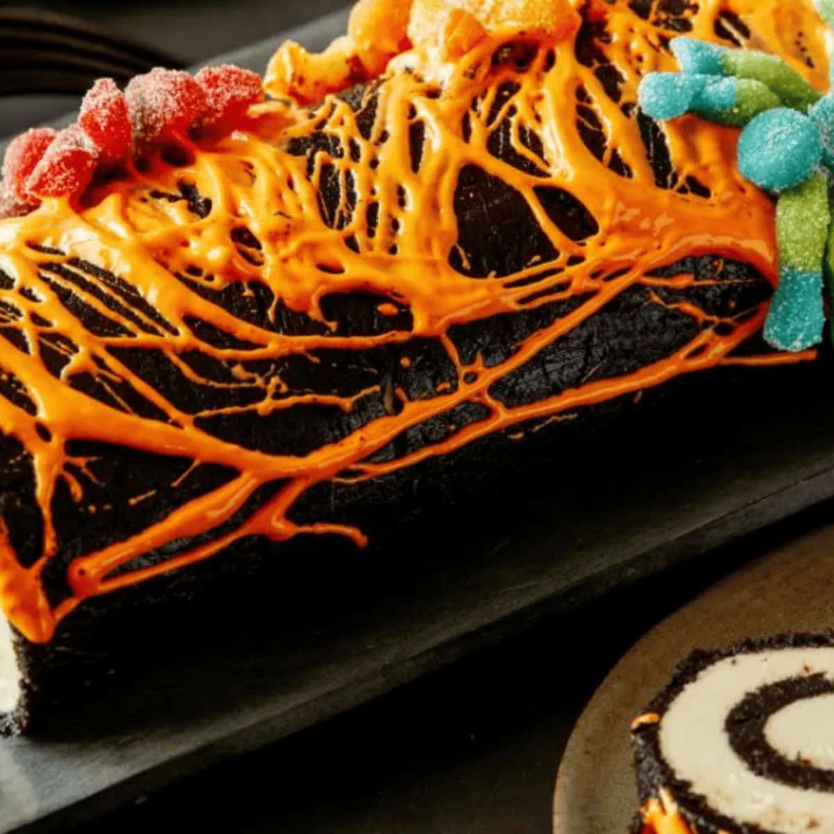 A Swiss roll that looks like a log with orange spiderwebs and spiders on top.