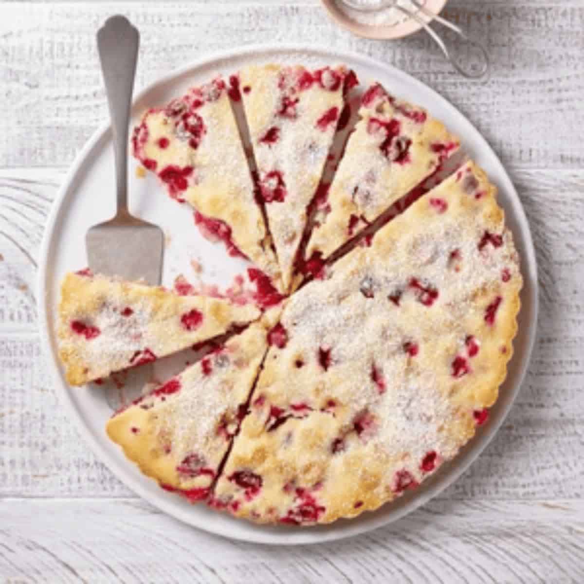 A beautifully sliced Nantucket cranberry tart, featuring a flaky golden crust filled with vibrant cranberry filling, garnished with a dusting of powdered sugar.