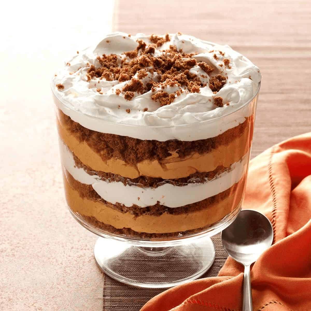 A festive Pumpkin-Butterscotch Gingerbread Trifle, showcasing layers of moist gingerbread, creamy pumpkin pudding, and rich butterscotch sauce, topped with whipped cream and a sprinkle of cinnamon, served in a clear glass trifle dish to highlight its colorful layers.
