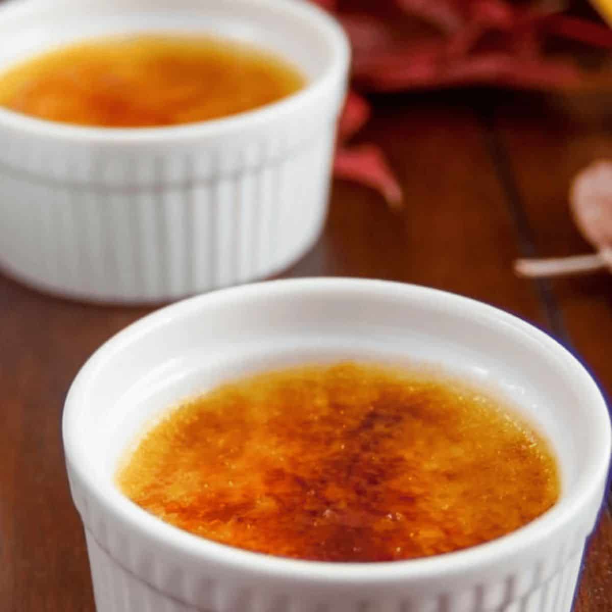 A rich pumpkin crème brûlée, featuring a smooth, spiced pumpkin custard topped with a perfectly caramelized sugar crust, garnished with a sprinkle of cinnamon.