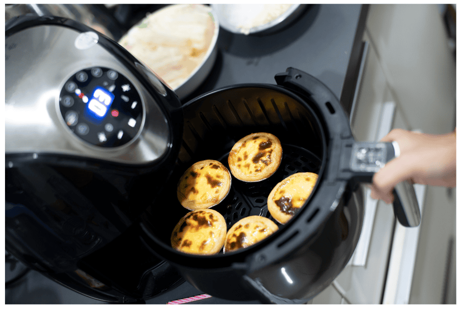 An air fryer with its basket partially opened to reveal baked goods inside.