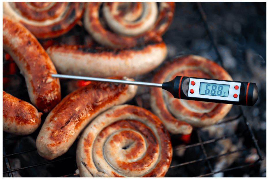 Sausages on a fire with a meat temperature thermometer showing the current temperature of the meat.