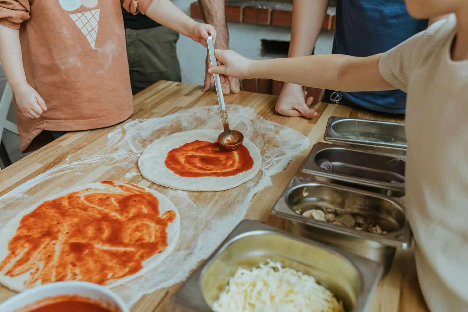 Kids placing tomato paste on a pizza base