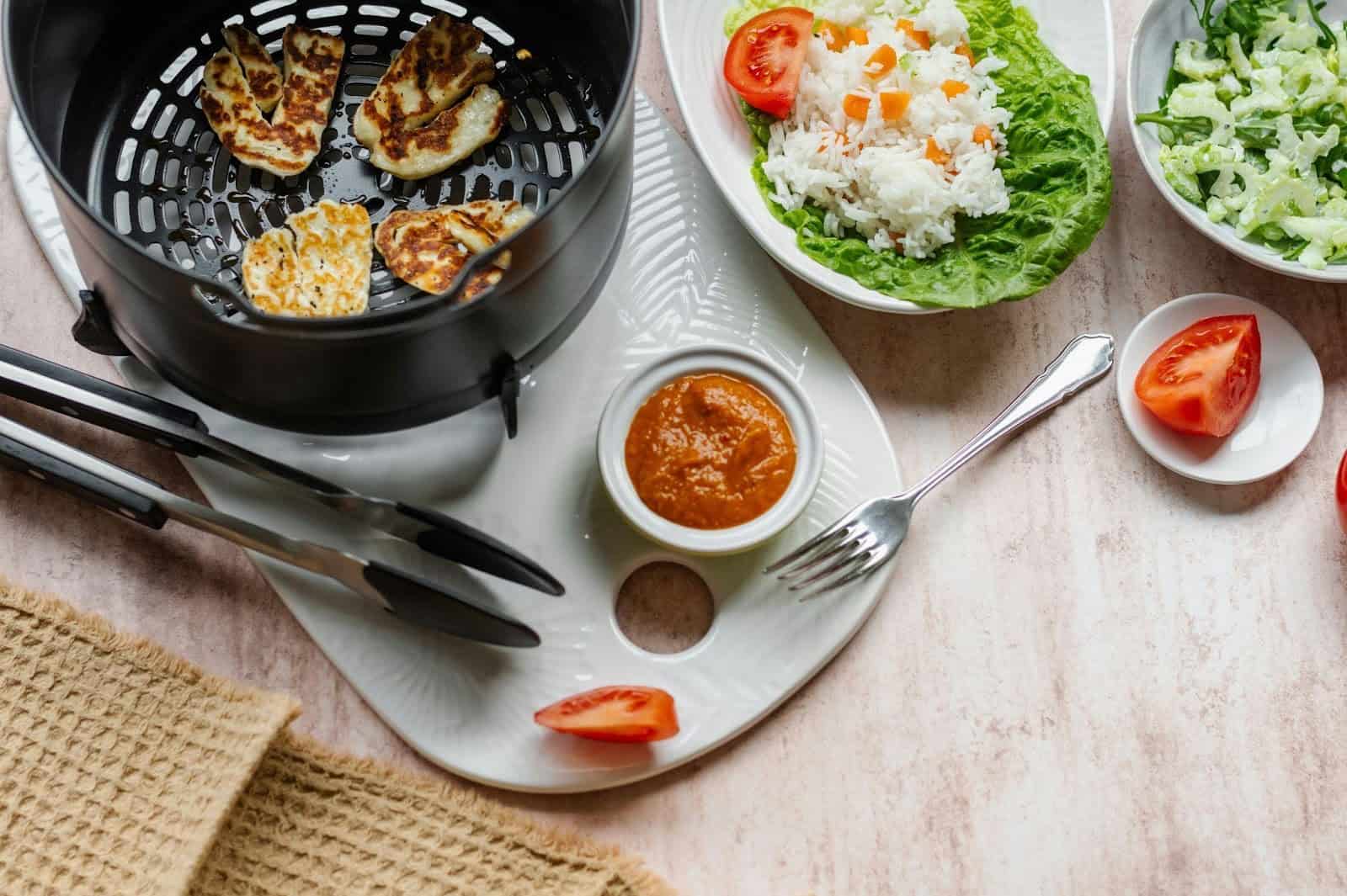 An air fryer basket with a few added ingredients alongside it, such as a piece of tomato, onions, rice, and more.