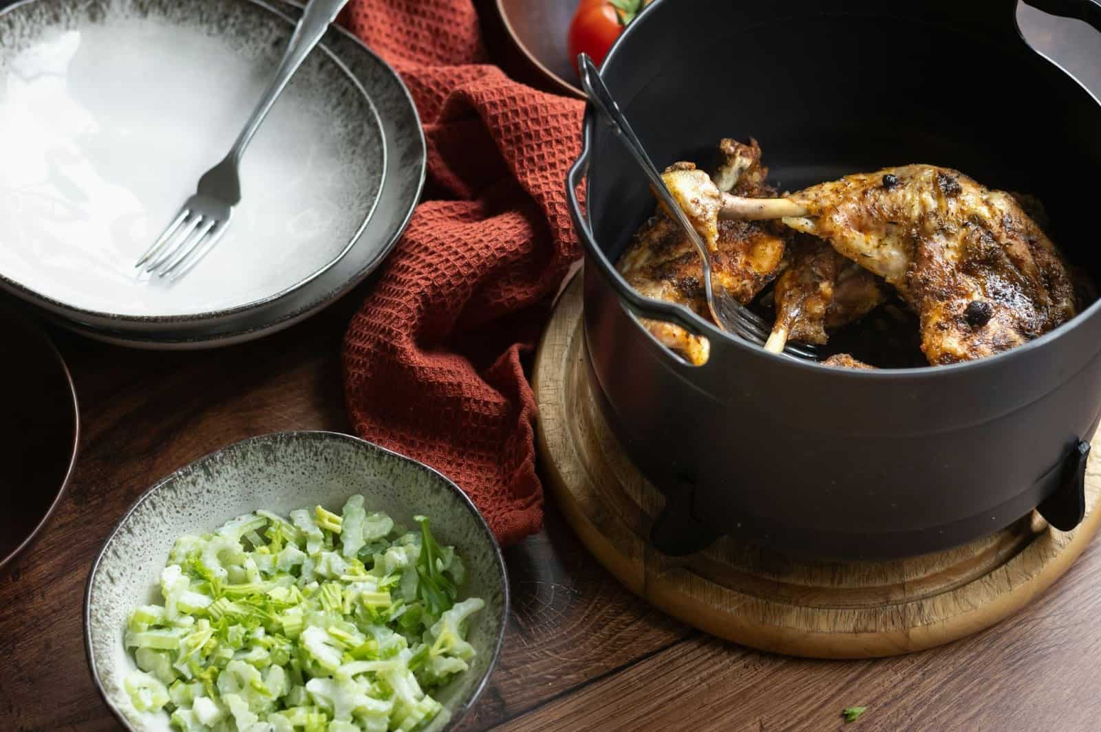 A pot with a cooked chicken, and a plate with ready sliced vegetables in it.