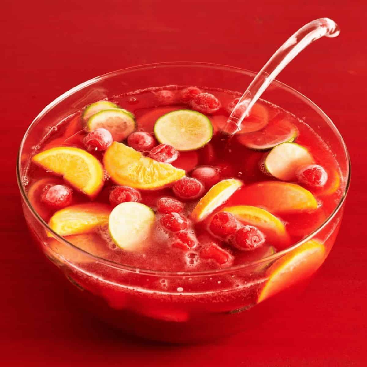 Cherry punch in a glass bowl with a glass ladle and freshly sliced lemon and whole cherries.