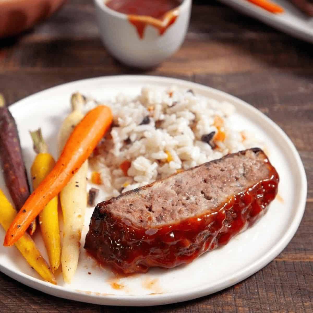 Classic meatloaf in a white plate with fresh veggies and cooked rice.