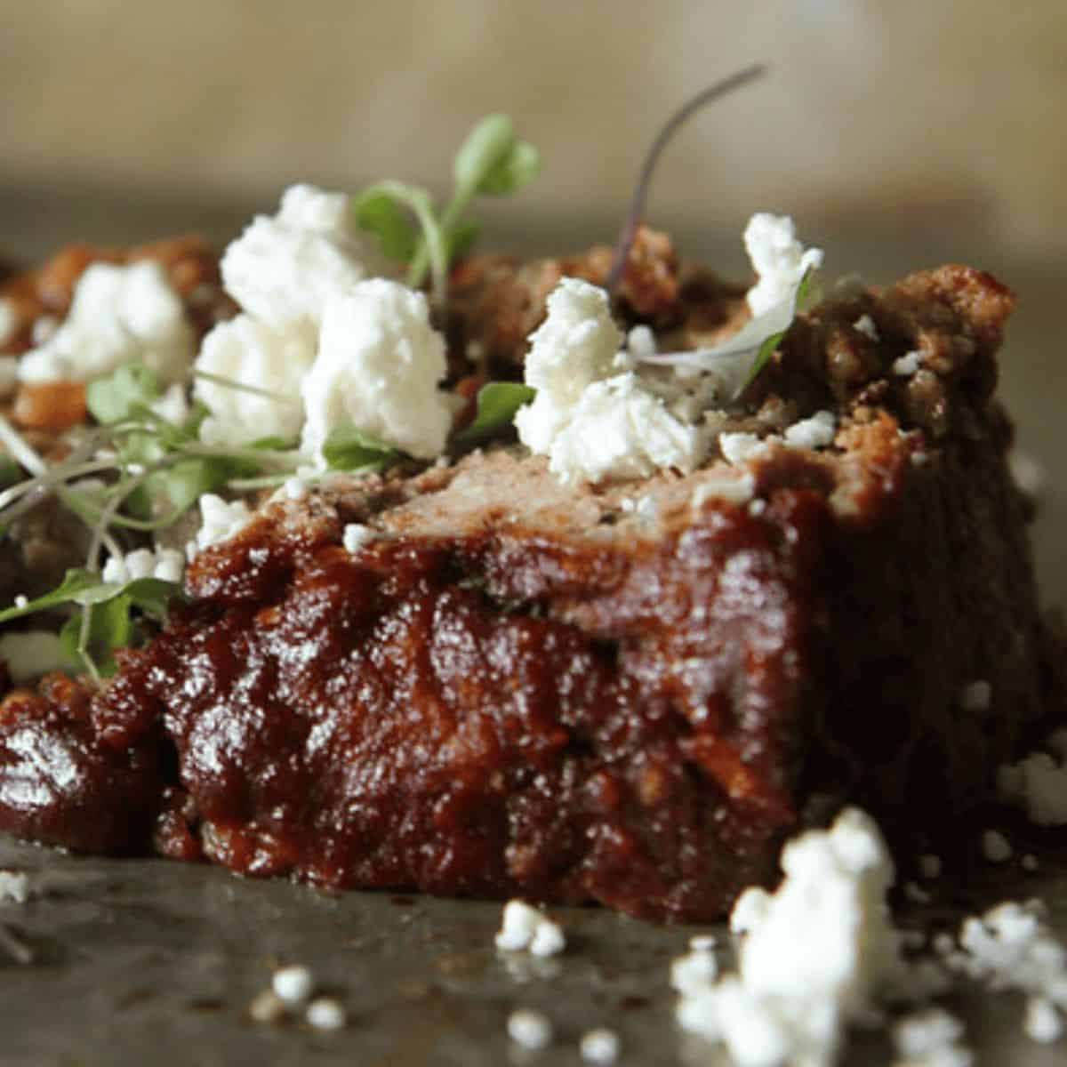 Greek Meatloaf slice sprinkled with feta cheese and a sprig of fresh herbs as a decorative garnish.
