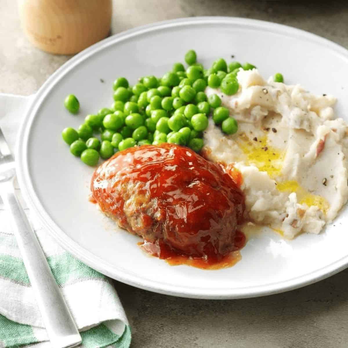 An appetizing meal featuring lil cheddar meatloaf, and mashed potatoes and peas.