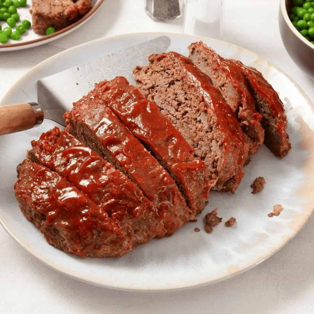 Slow cooker meatloaf on a white plate with a lifter on the side.