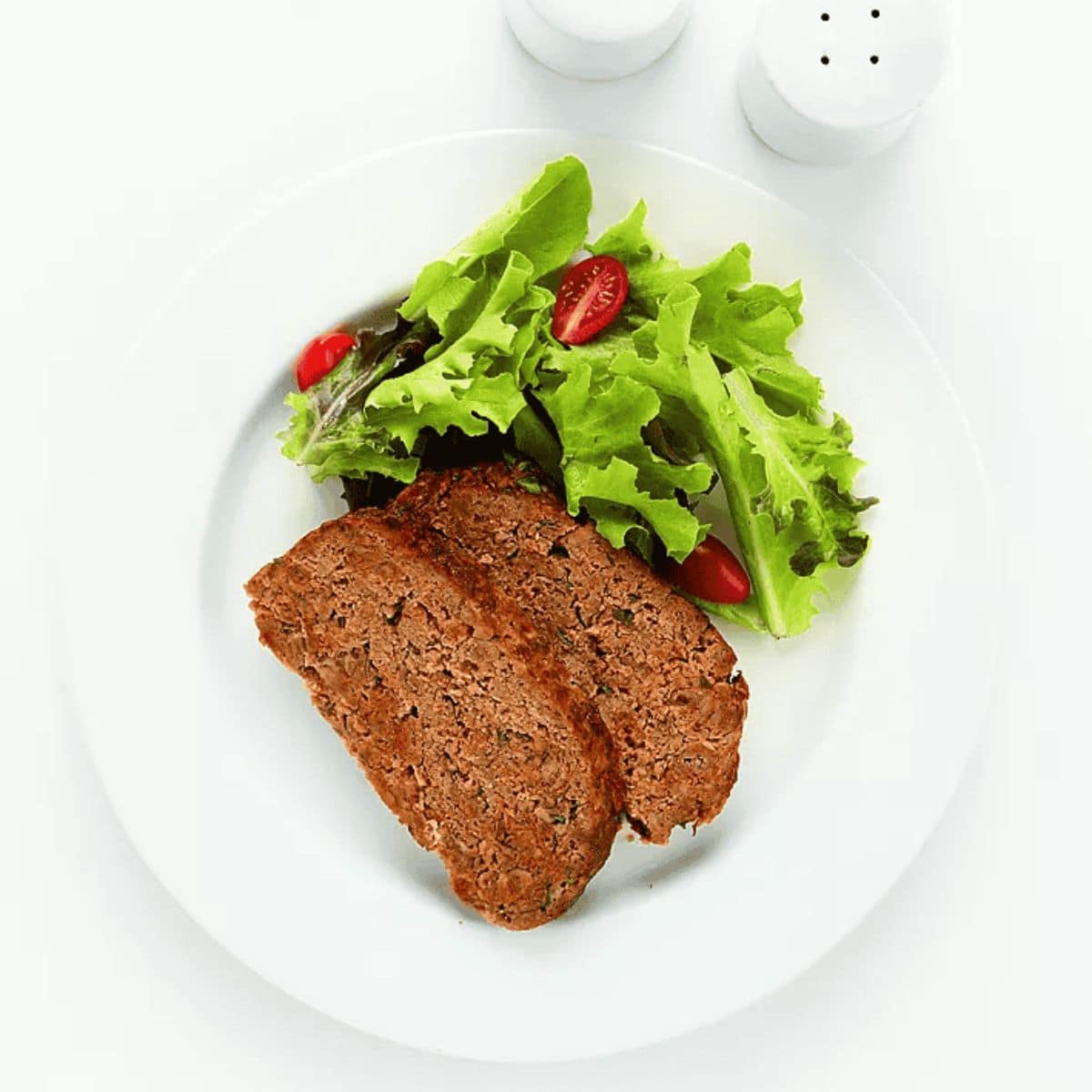 A devouring meal with parmesan meatloaf, with some fresh greenery on the side as a garnish.