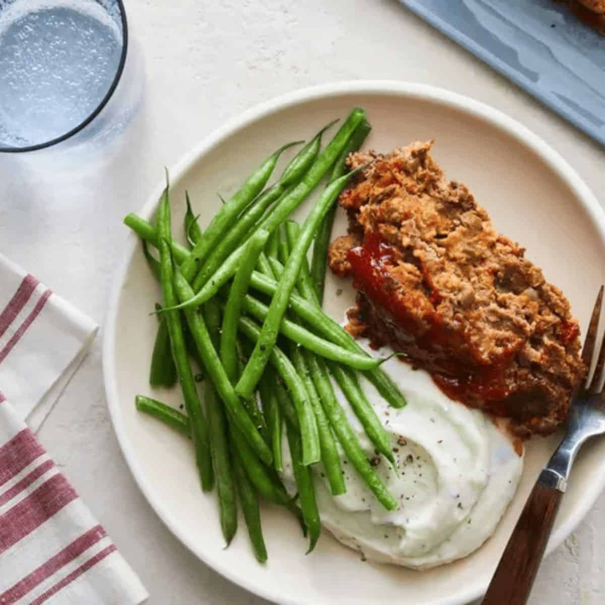 An appetizing meal featuring southern meatloaf, mashed potatoes, and green beans on the side.