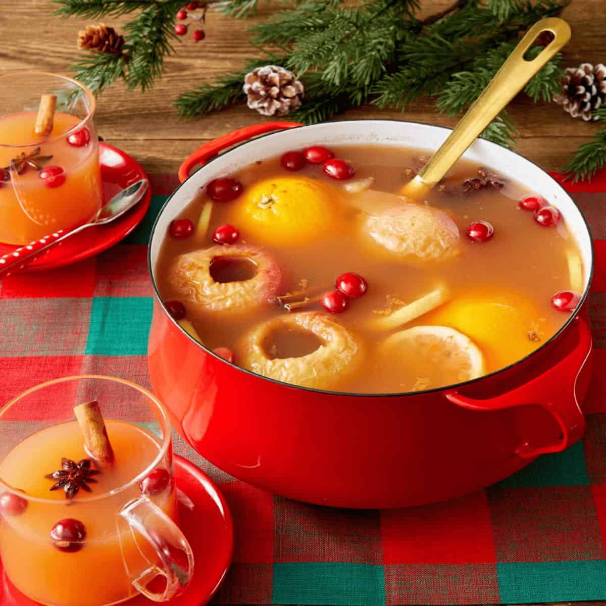 A refreshing drink with wassail in a red pot with whole oranges in it.