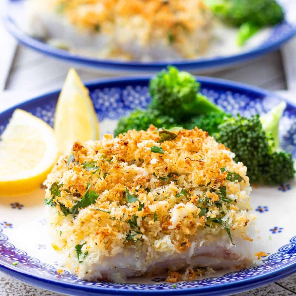 A flavorful meal with baked cod with parmesan crust served with brocolli and sliced lemon in a dish. 