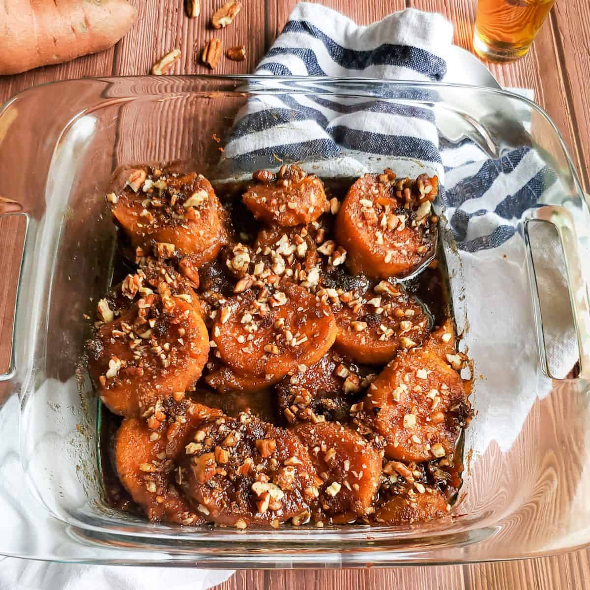 Bourbon-Spiked candied Sweet Potatoes in a clear glass dish set on a table.