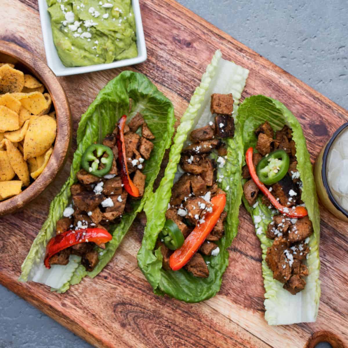 A yummy meal with carne asada tacos in a wooden tray with a side dip. 