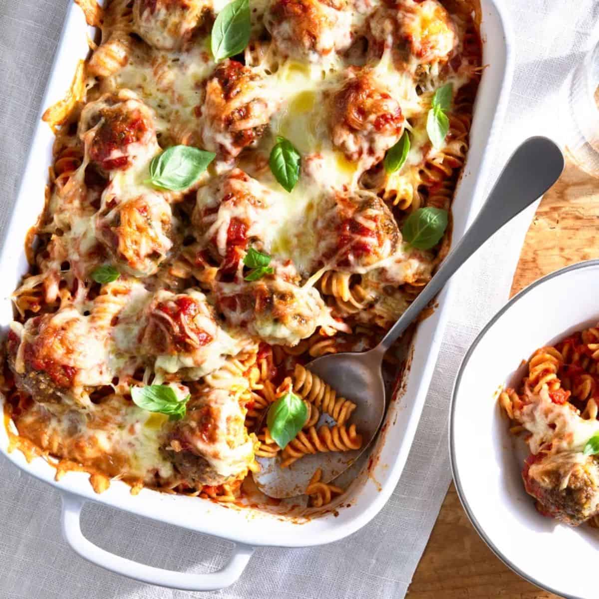 A yummy meal with cheesy meatball casserole ina white dish with a metal spoon. 