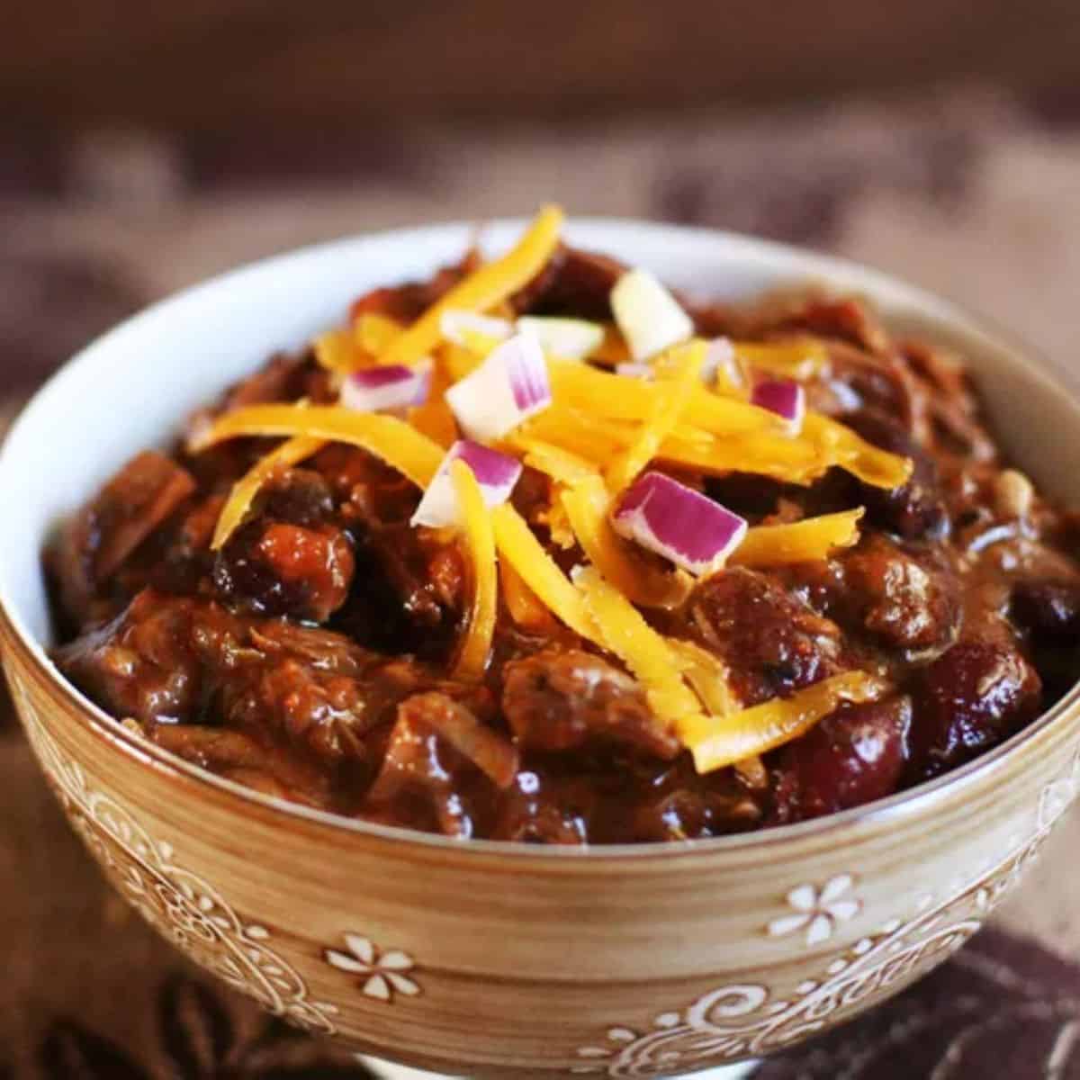 A hearty bowl of Chili Con Carne with beans, ground beef, and spices, garnished with toppings like grated cheese.
