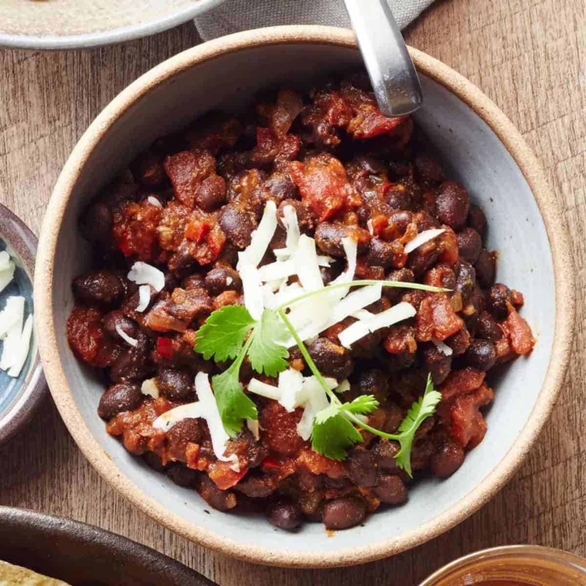Vegetarian chili in a dish sprinkled with fresh herbs and cheese as a garnish.
