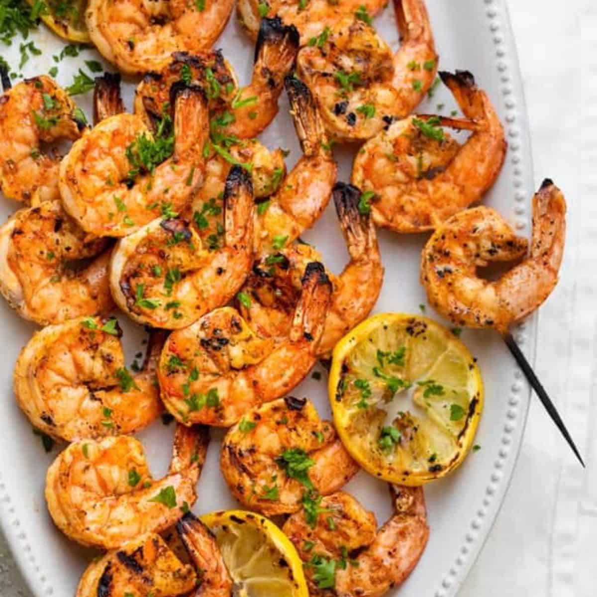 Grilled shrimp skewers with grilled sliced lemon served in a wide dish. 