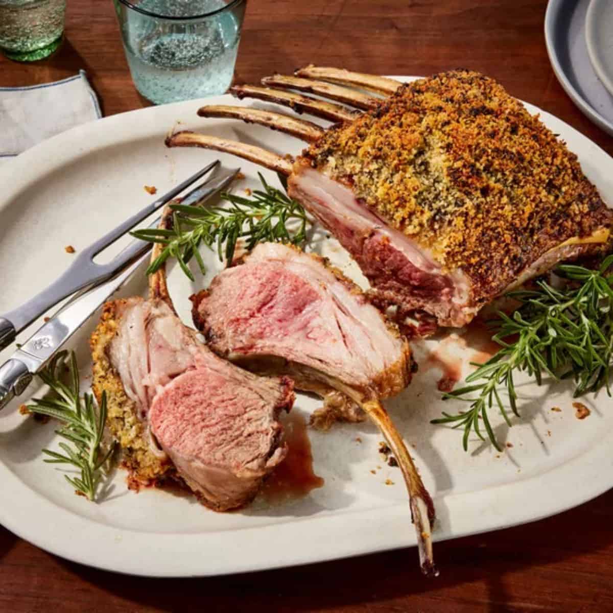 Roasted rack of lambs served in a plate with a silver knife and fork.