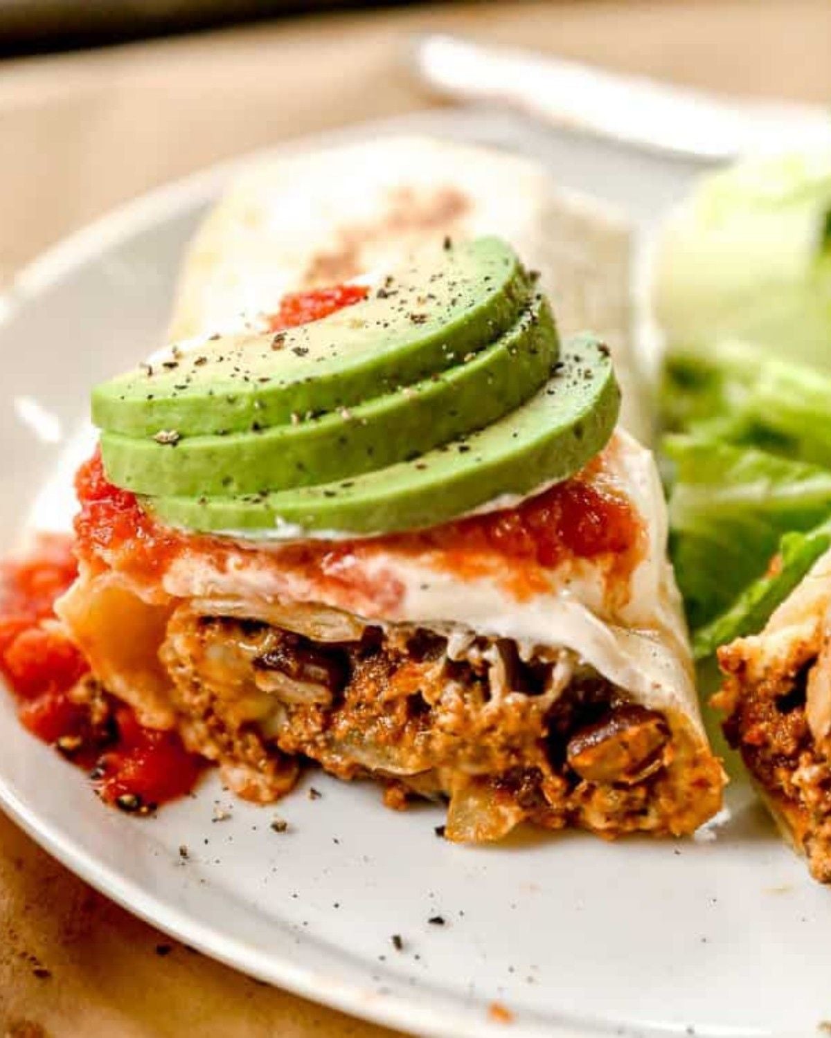 Easy ground beef burrito topped with sliced avocado, salsa, and sour cream on a white plate for a quick dinner recipe