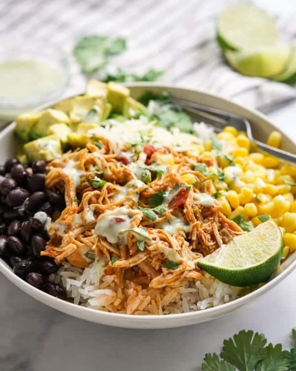 Slow-Cooker Chicken Burrito Bowl in a white bowl with rice, black beans, corn, avocado, and lime
