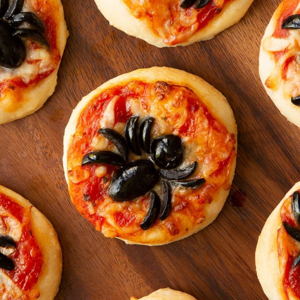 Mini Halloween spider pizzas decorated with black olive spiders on a wooden board.